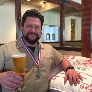 Chama River brewer Zach Guilmette poses with his GABF gold medal and Class VI Golden Lager. (Photo courtesy of Chama River)